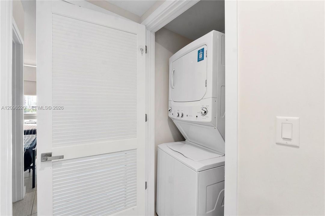 Stacked laundry unit with white finished cabinetry and a louvered door featuring a brushed metal lever handle