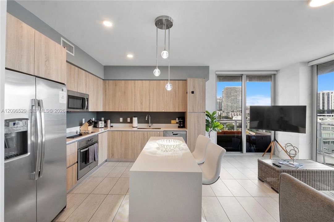 Kitchen featuring light-finish cabinetry, a central island with a solid-surface countertop, stainless steel appliances, modern pendant lighting, and ceramic tile flooring