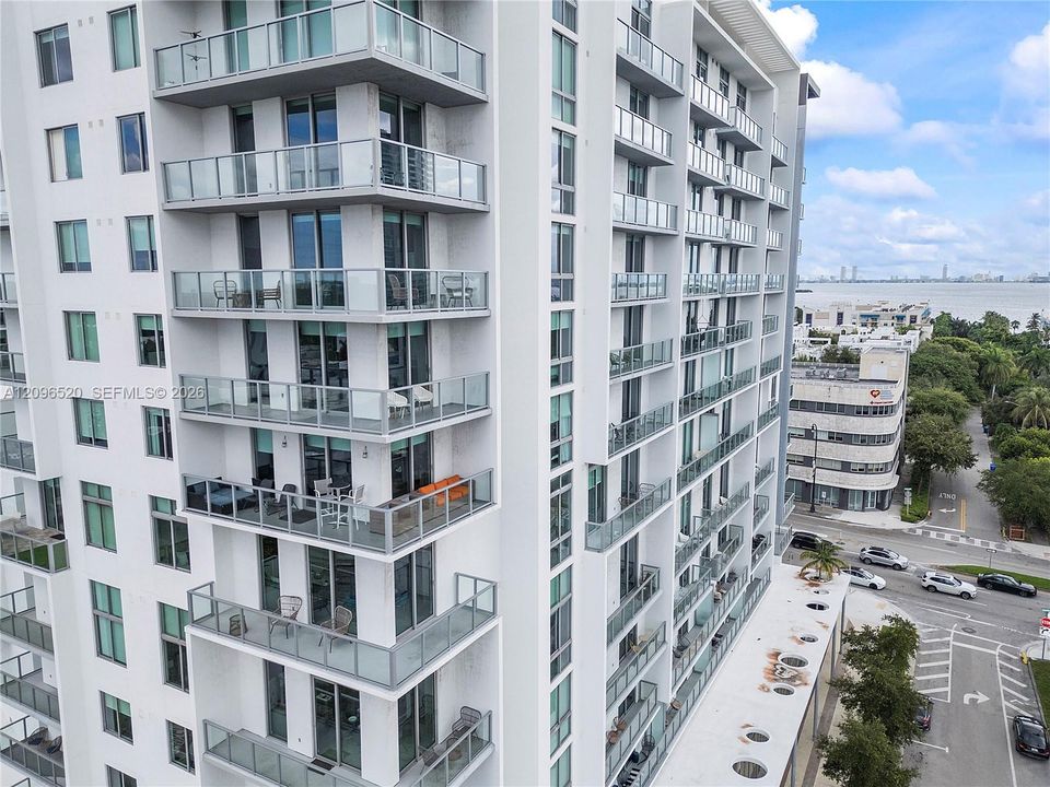 High-rise residential exterior featuring stacked private glass-railed balconies, floor-to-ceiling windows, and white concrete facade