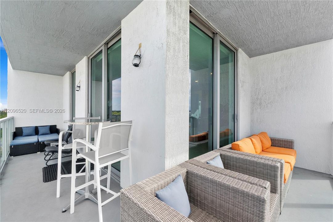 Covered balcony featuring concrete flooring, floor-to-ceiling glass sliding doors, and wall-mounted exterior lighting