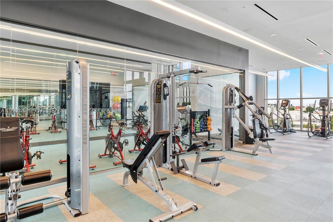 Fitness center featuring floor-to-ceiling windows, mirrored walls, recessed linear lighting, and large-format tile flooring