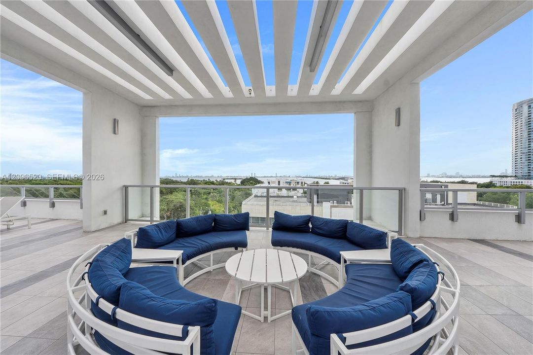Covered rooftop terrace featuring a pergola-style ceiling, large-format tile flooring, and glass panel railings