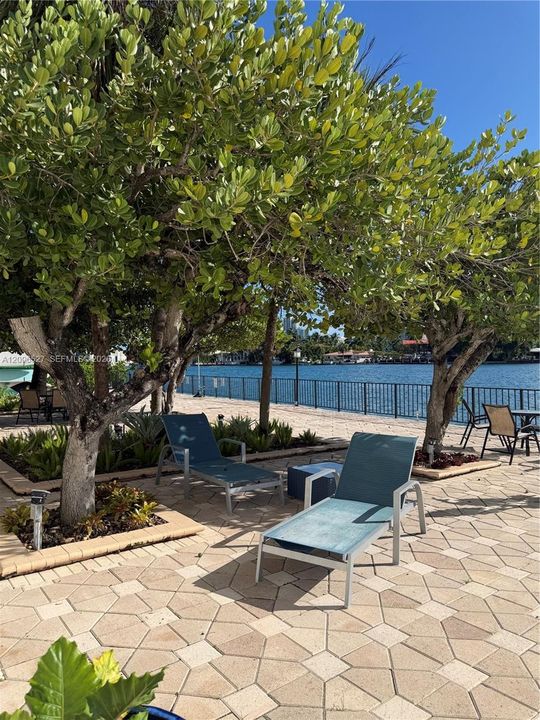Waterfront terrace featuring geometric paver hardscaping, mature shade trees, and a metal perimeter railing