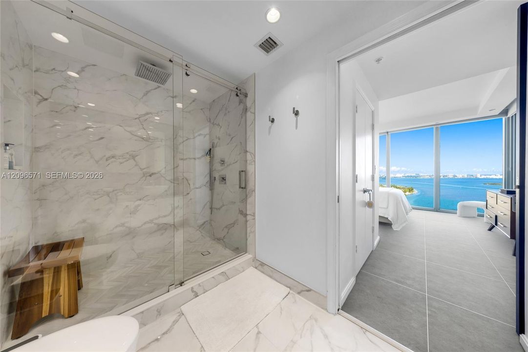 Walk-in shower with floor-to-ceiling veined tile, frameless glass enclosure, rain-style showerhead, and integrated wall niche