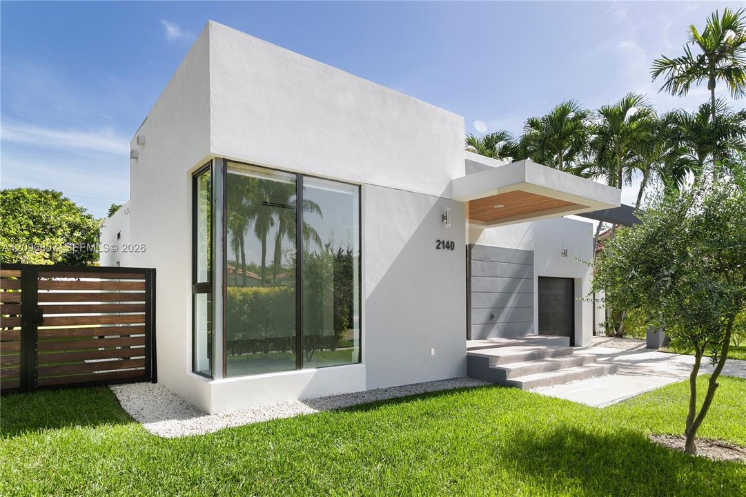 Modern exterior featuring a smooth stucco finish, floor-to-ceiling corner glazing, a wood-paneled cantilevered entryway, horizontal slat fencing, and concrete step entrance