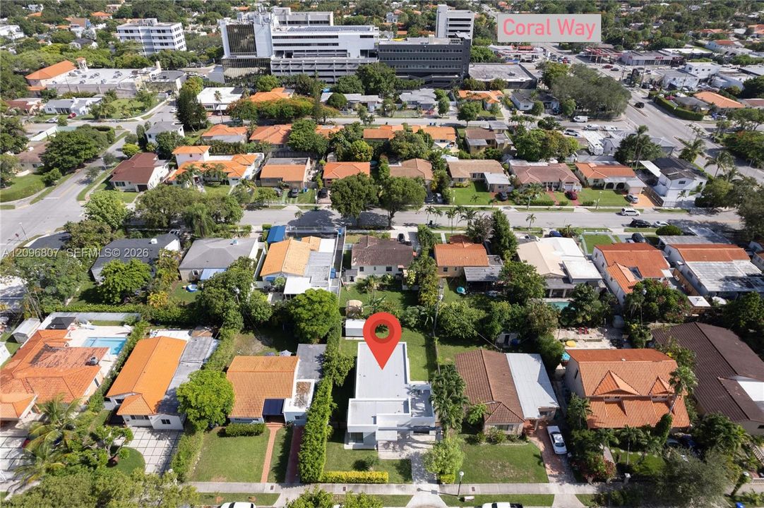 Aerial perspective of residential property featuring a flat roof structure, grass lawn, and dense perimeter landscaping