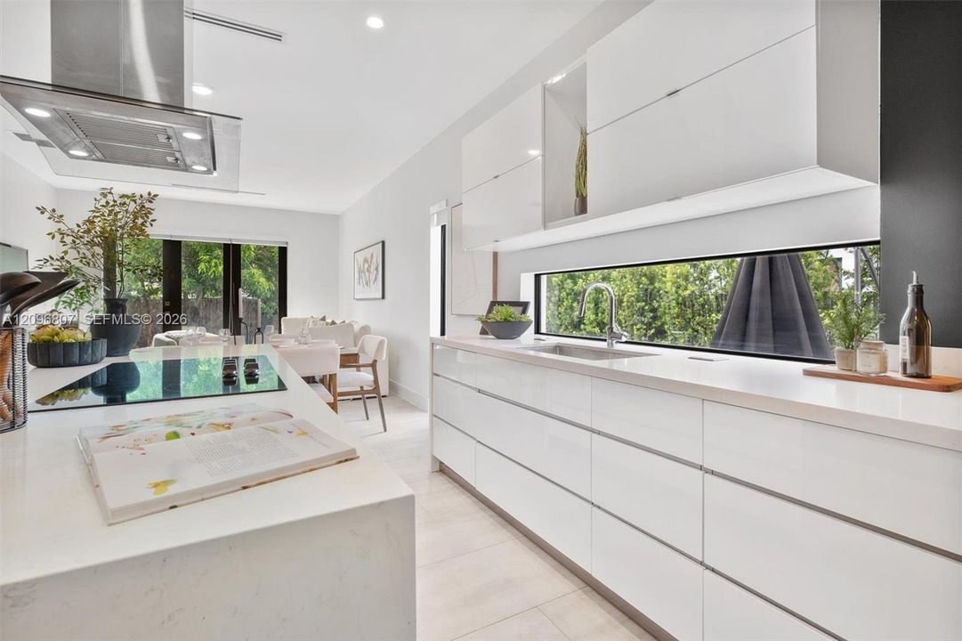 Contemporary kitchen featuring flat-panel high-gloss cabinetry, stone-surface countertops, a full-width horizontal backsplash window, a stainless steel undermount sink, and a stainless steel ceiling-mounted range hood