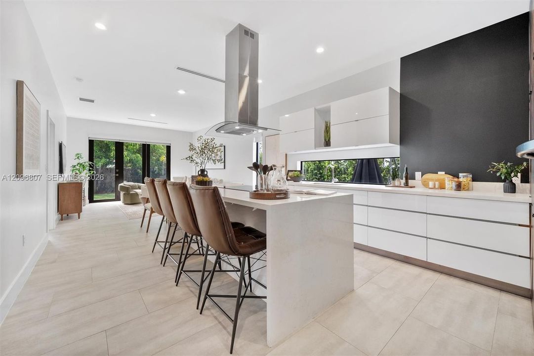 Kitchen featuring a large central island with quartz countertops, minimalist high-gloss white cabinetry, a stainless steel chimney-style range hood, and porcelain tile flooring