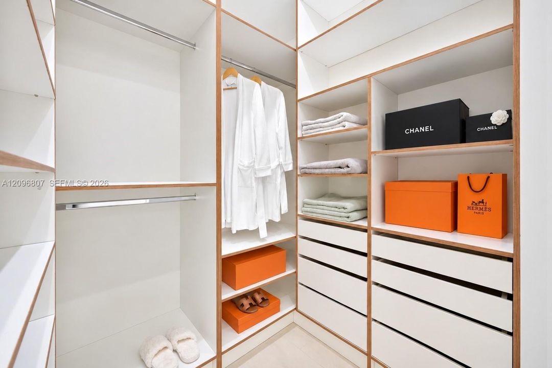 Custom walk-in closet featuring floor-to-ceiling white shelving with wood-tone edging, multiple integrated drawers, and dual-level metal hanging rods