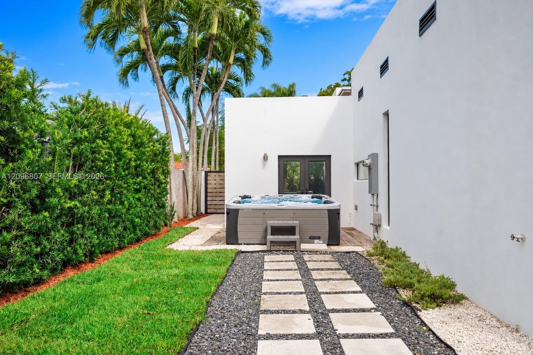Outdoor space featuring a standalone spa, stone paver walkway with gravel surround, manicured lawn, and mature palm trees