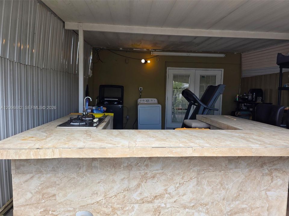 Spacious covered patio featuring a built-in bar, cooktop, sink, generous counter space, and bar seating—ideal for outdoor entertaining.