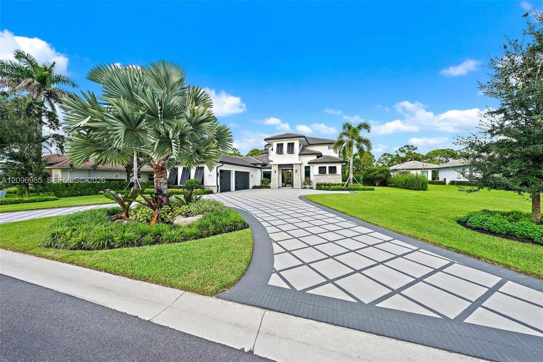 Multi-level exterior featuring a patterned concrete paver driveway, white stucco facade, multi-car garage, and professionally landscaped lawn with mature palm trees