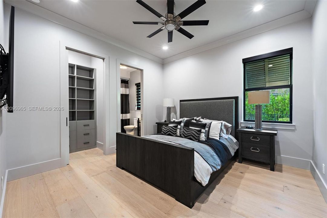 Room featuring wood-finish flooring, tray ceilings with recessed lighting, a multi-blade ceiling fan, and built-in closet shelving