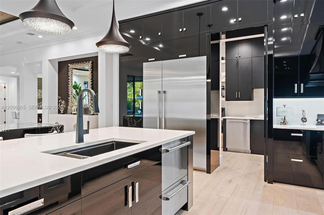 Kitchen featuring high-gloss black cabinetry, white quartz countertops, stainless steel built-in refrigerator, wood-finish flooring, and pendant lighting