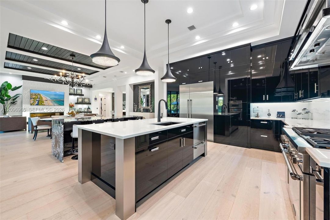 Chef's kitchen featuring high-gloss black cabinetry, a central island with a stone countertop, wood-finish flooring, integrated stainless steel appliances, and three-tier pendant lighting