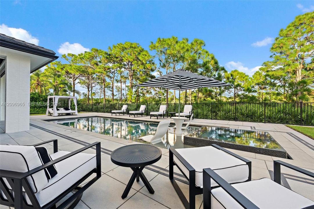 Backyard featuring a paved stone pool deck, rectangular swimming pool, integrated spa, and metal perimeter fencing