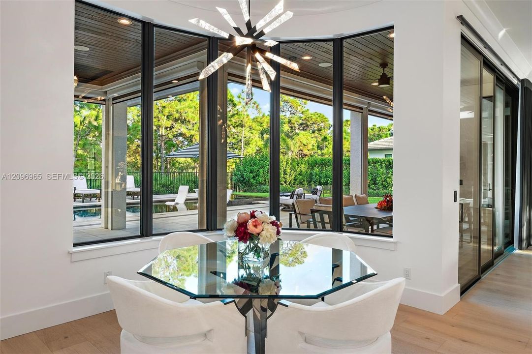 Curved floor-to-ceiling window wall featuring black mullions, expansive wood-finish flooring, recessed ceiling lighting, and a modern geometric pendant chandelier