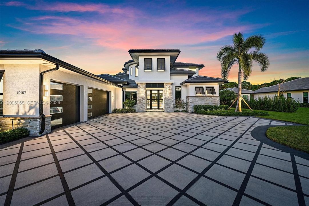 Modern multi-level exterior featuring a patterned concrete paver driveway, stone veneer accents, multi-car garage with glass-panel doors, and a tiled roof