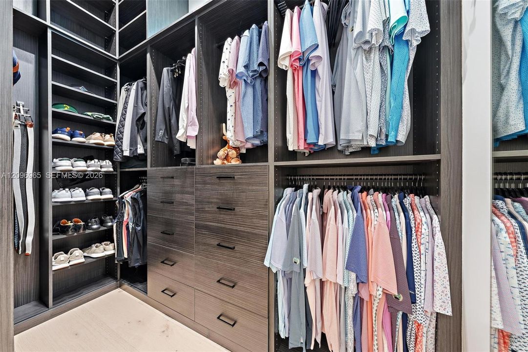 Custom walk-in closet featuring floor-to-ceiling built-in cabinetry, dark wood-finish shelving, integrated hanging rods, and multiple soft-close drawers with matte black hardware