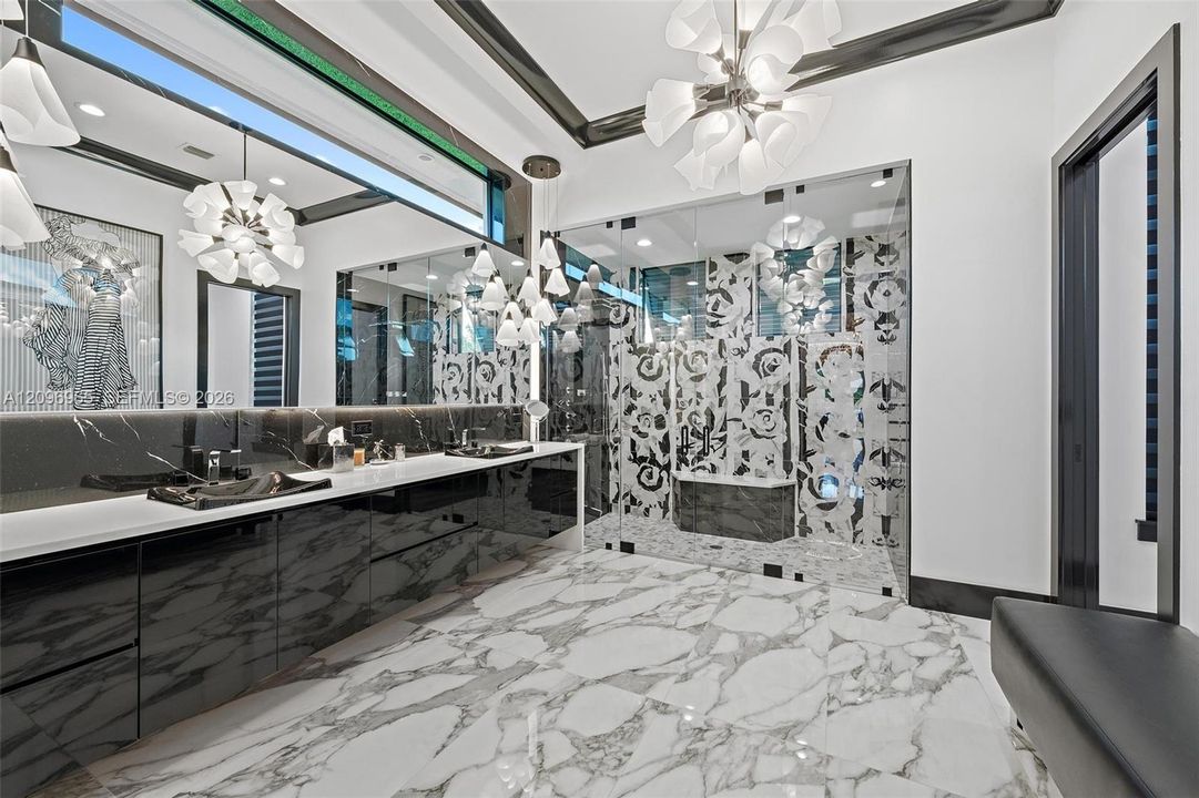 Bathroom featuring high-gloss black cabinetry, white stone-finish countertop, dual integrated sinks, glass-enclosed shower with patterned tile, and large-format tile flooring