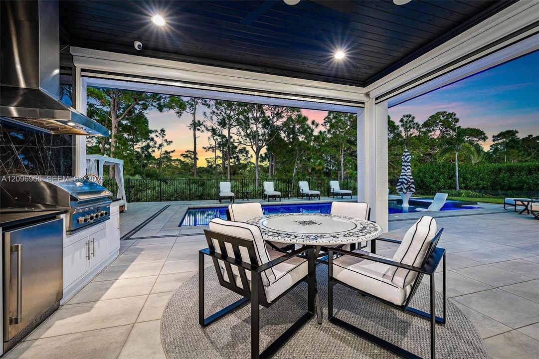 Covered outdoor kitchen featuring built-in stainless steel appliances, tiled flooring, recessed ceiling lighting, and direct access to an in-ground swimming pool
