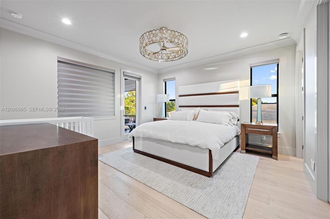 Neutral-toned bedroom featuring wood-finish flooring, recessed lighting, a decorative circular ceiling fixture, and a glass-paneled door