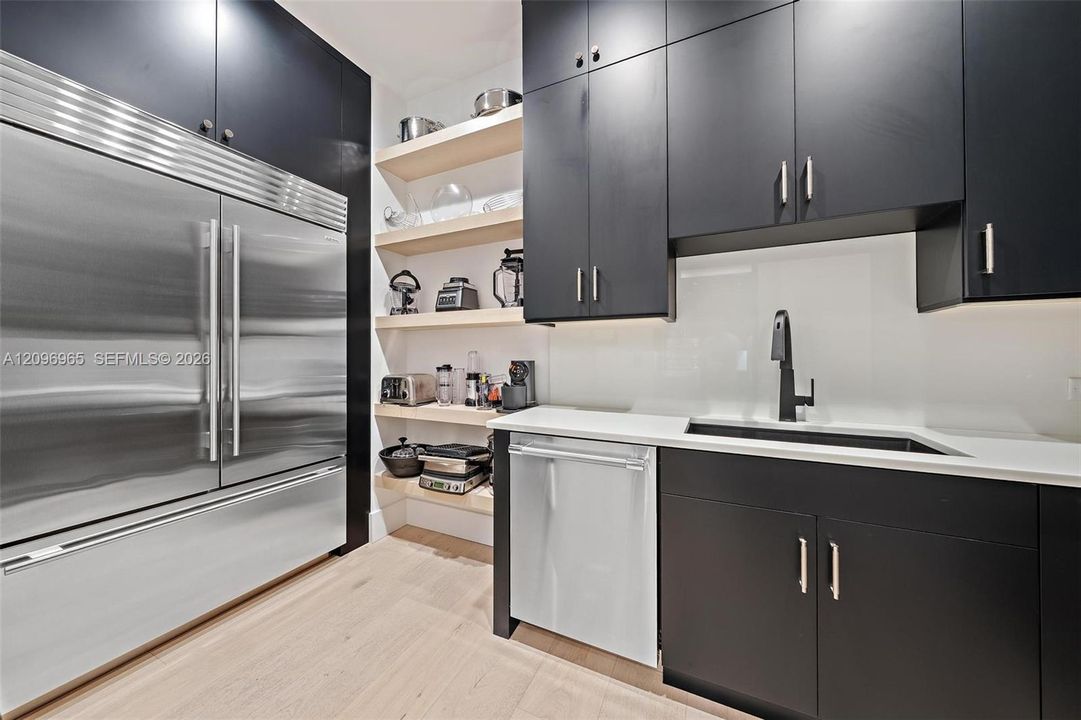 Custom matte black cabinetry, stainless steel professional-grade refrigerator and dishwasher, solid-surface countertops, integrated sink with a matte black faucet, and natural wood-finish open shelving