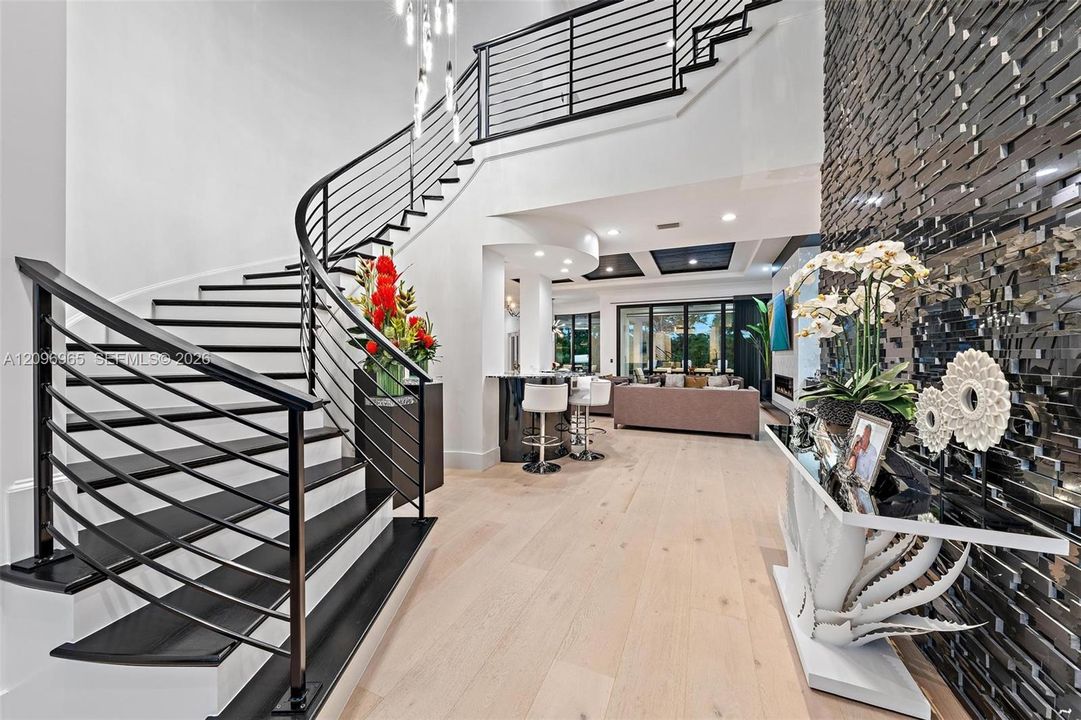 Grand foyer featuring a curved staircase with black metal railings, light wood-finish flooring, a textured black stone accent wall, and recessed ceiling lighting