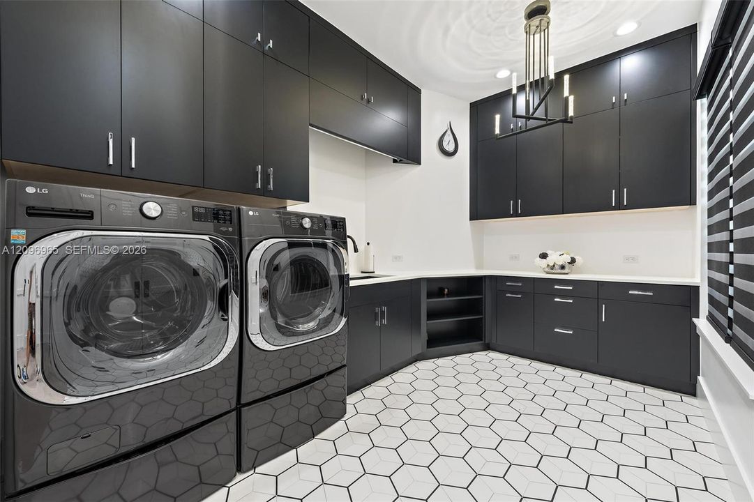 Laundry area featuring ceiling-height charcoal cabinetry, quartz countertops, integrated under-mount sink, geometric tile flooring, and a modern tiered chandelier