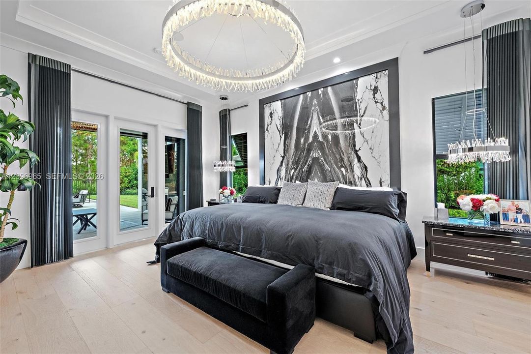 Tray ceiling featuring a large circular crystal chandelier, expansive stone-finish accent wall with dark veining, light wood-finish flooring, and multi-panel glass doors