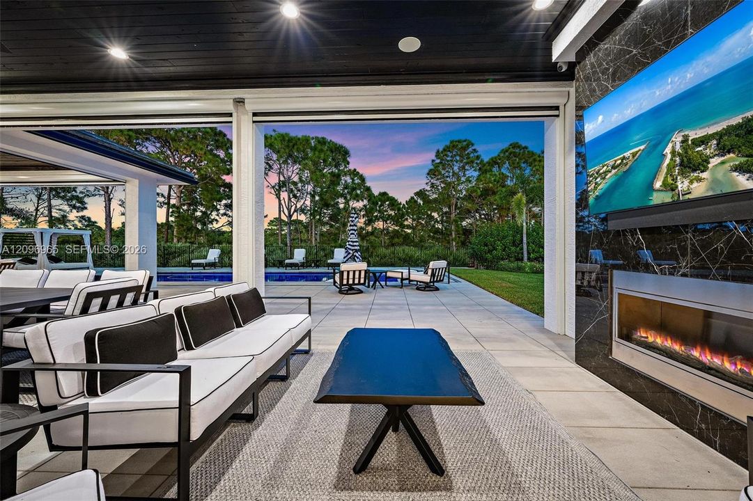 Covered outdoor living space featuring a linear gas fireplace, wall-mounted television, recessed lighting, and large-format tile flooring