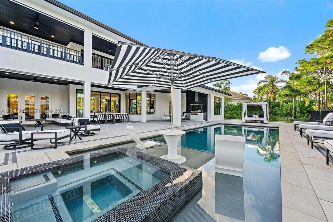 Expansive outdoor living area featuring a custom swimming pool with an integrated spa, tiled pool deck, covered patio space, and exterior kitchen