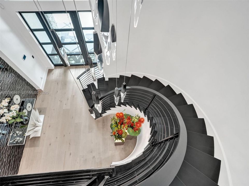 Curved staircase featuring dark treads, black metal railing, floor-to-ceiling glass-paneled door, modern multi-pendant light fixture, and wood-finish flooring
