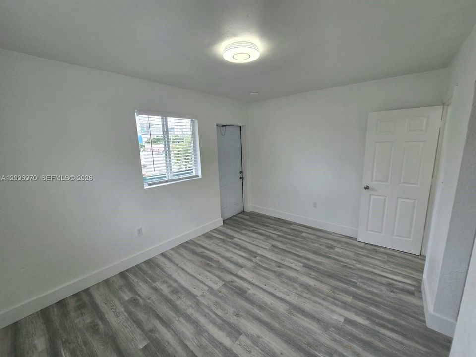Interior space featuring neutral wall paint, wood-finish flooring, a flush-mount circular ceiling light, a multi-pane window, and a six-panel door