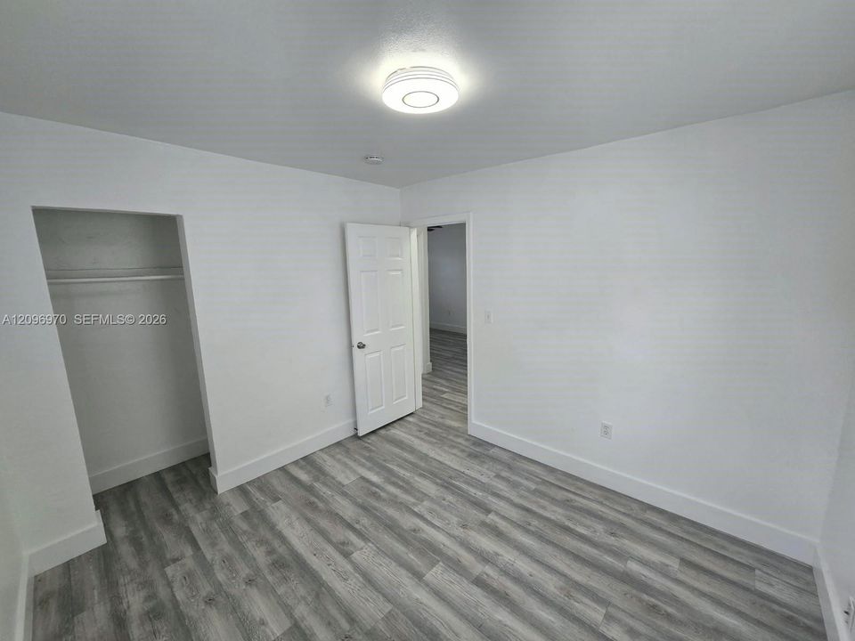 Neutral interior room featuring wood-finish flooring, a six-panel interior door, a built-in closet with overhead shelving, and a circular flush-mount ceiling light fixture