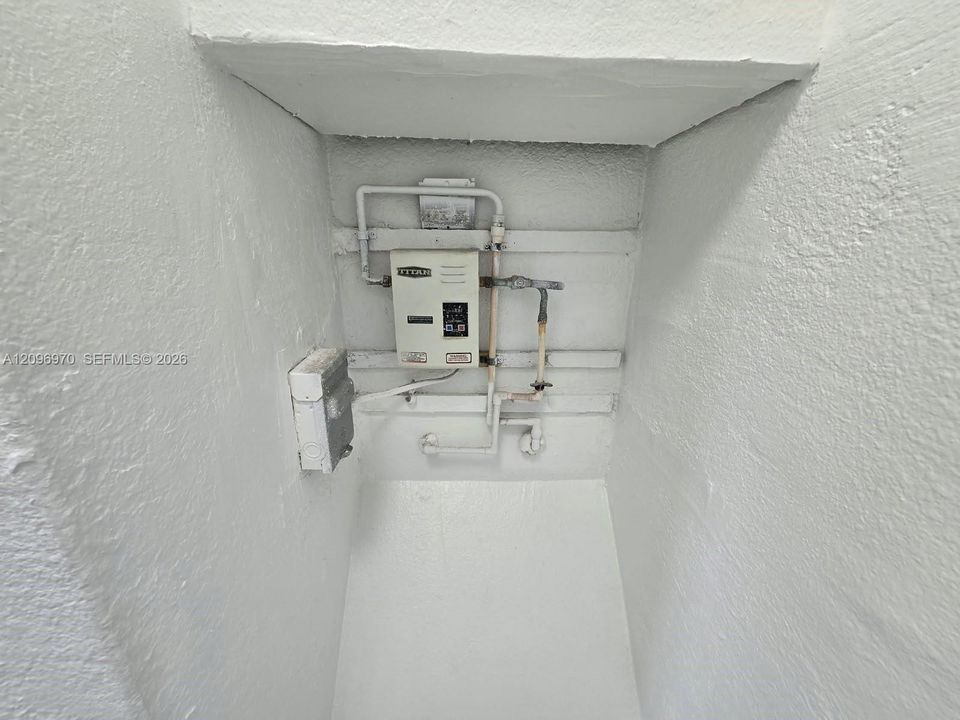 Electric tankless water heater with dedicated electrical disconnect and exposed plumbing conduits housed within a recessed utility alcove