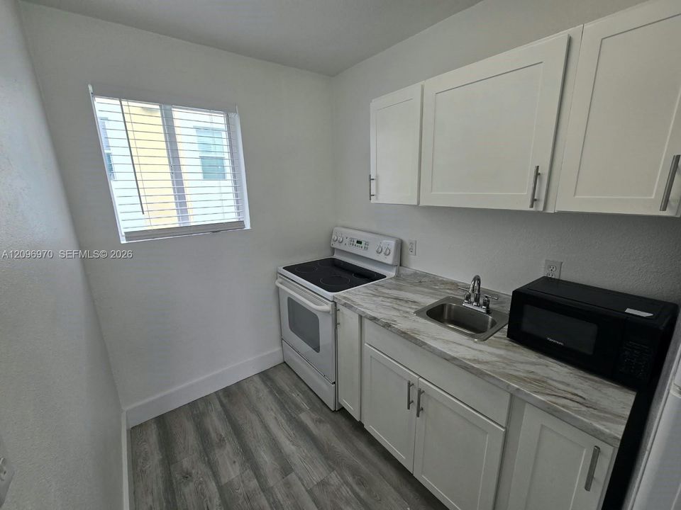 Kitchen featuring white shaker-style cabinetry, stone-patterned laminate countertops, stainless steel sink with pull-out faucet, and wood-finish flooring