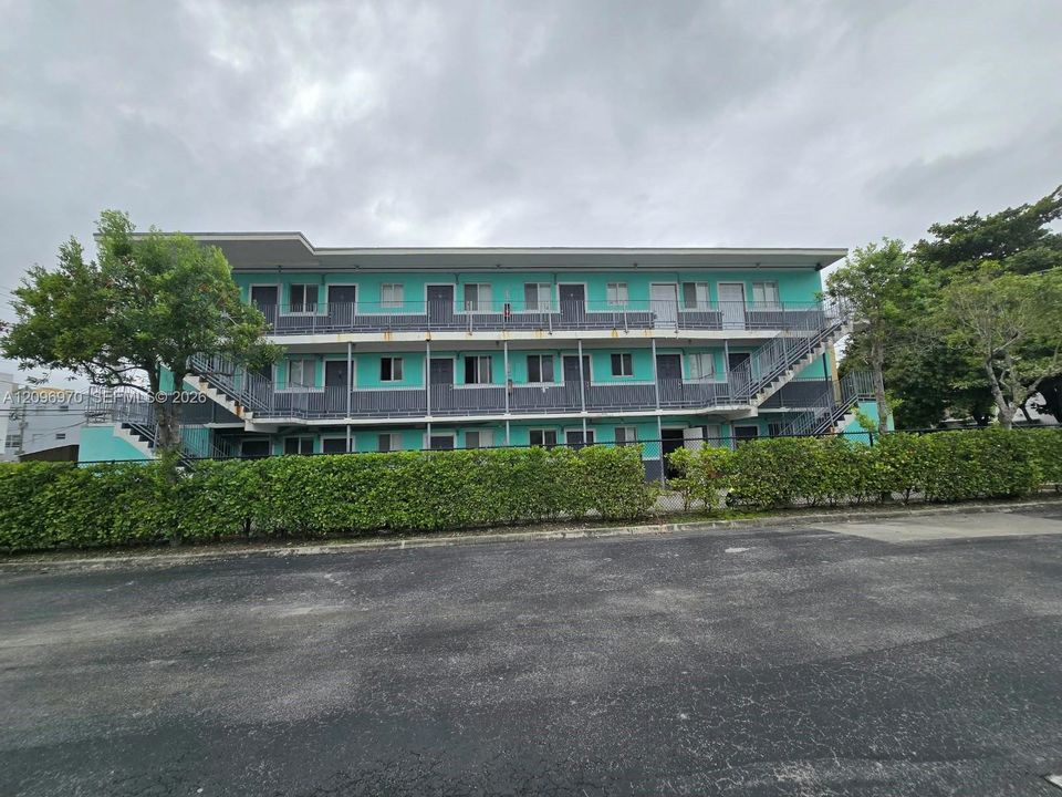 Multi-story building exterior featuring a teal and gray facade, metal staircases, exterior walkways, and mature landscaping