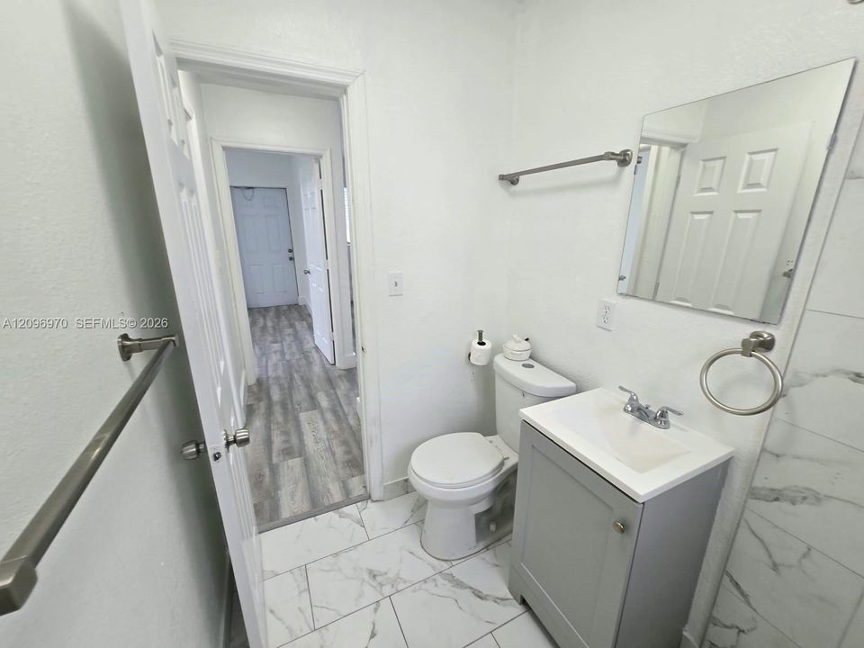 Bathroom featuring large-format tile flooring with a veined pattern, vanity with a rectangular sink, brushed nickel fixtures, and a wall-mounted mirror