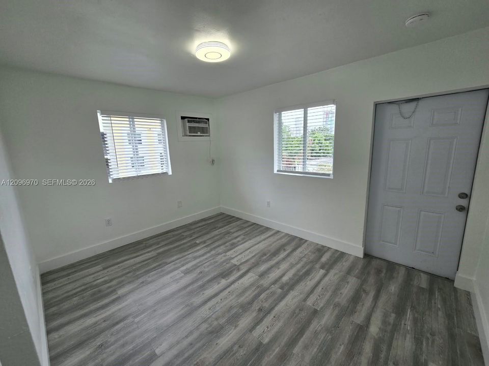 Interior space featuring wood-finish flooring, white walls, dual windows with blinds, a flush-mount ceiling light fixture, and a six-panel entry door