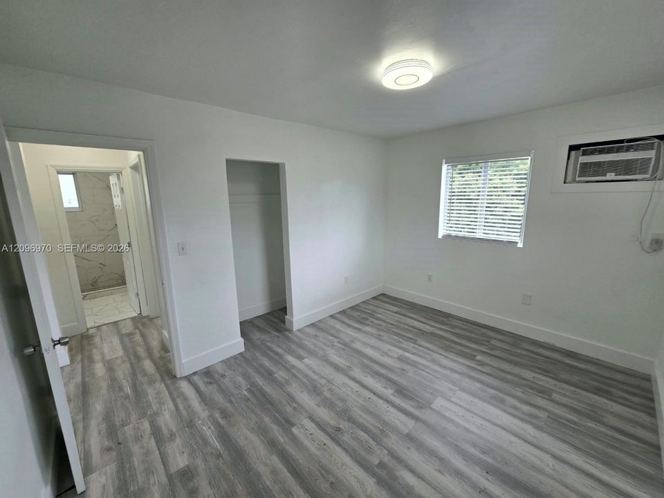 Room featuring wood-finish flooring, recessed LED lighting, a window with horizontal blinds, and a built-in wall air conditioning unit