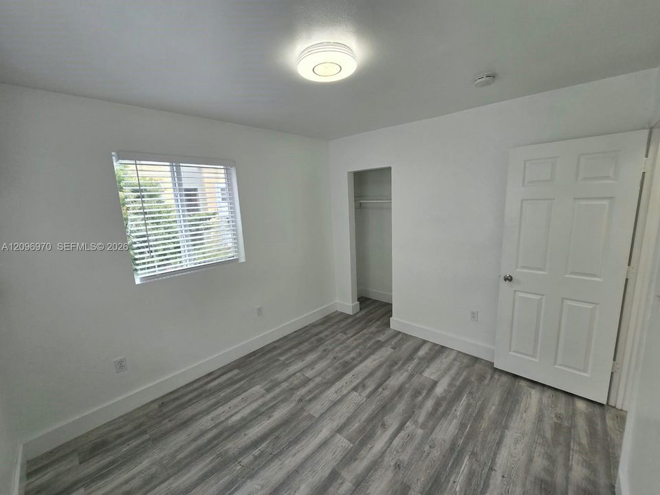 Interior space featuring wood-finish flooring, a recessed closet with built-in shelving, a flush-mount overhead light fixture, and a window with horizontal blinds