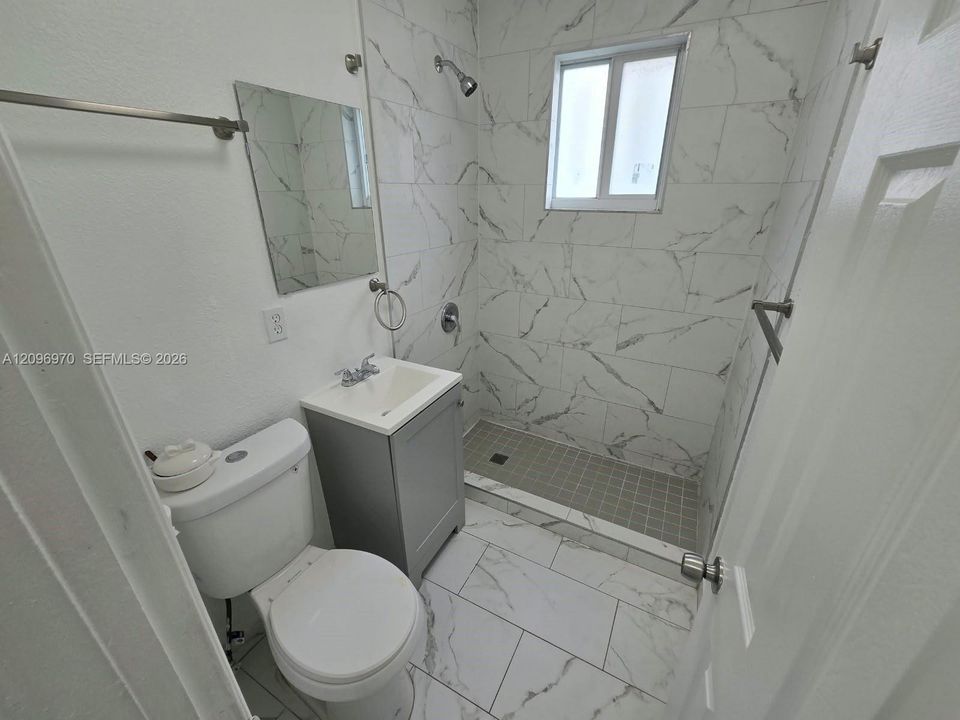Bathroom featuring floor-to-ceiling large-format tile with veining, grey vanity cabinet, white sink basin, and glass-paneled walk-in shower