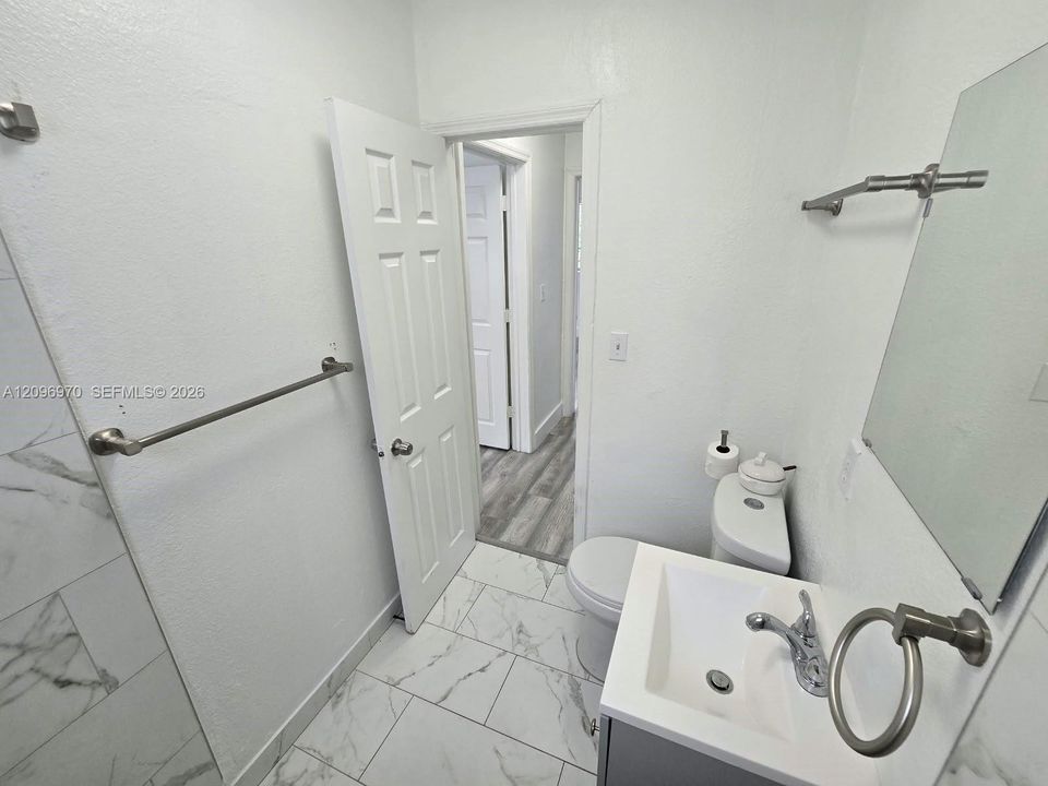 Bathroom featuring large-format tile flooring with a marble-finish, a vanity with a white rectangular basin and metal fixtures, and a shower surround with marble-finish tiling