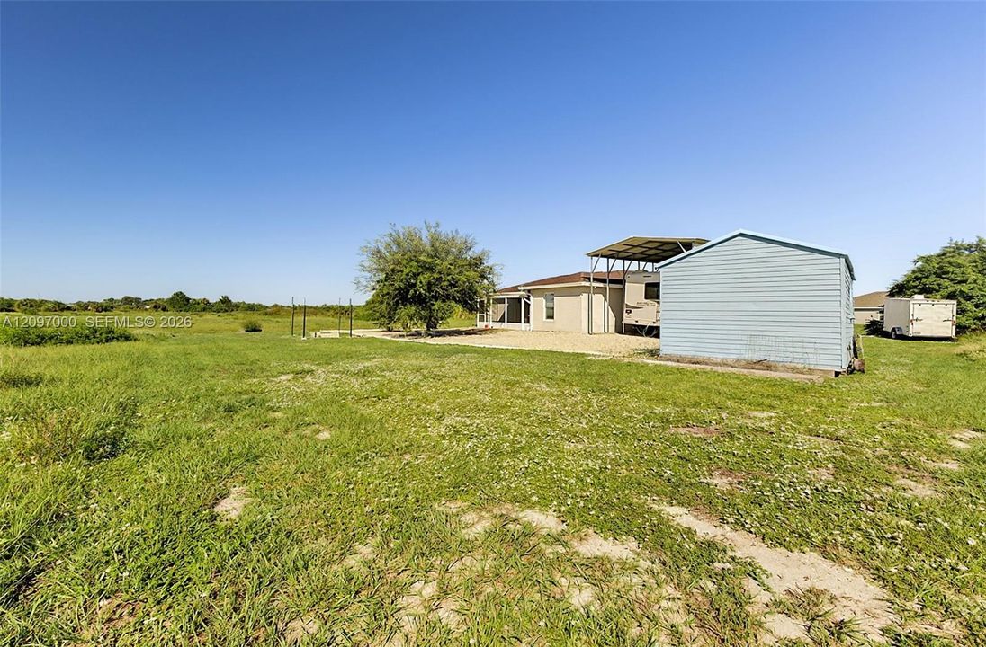 Expansive lot featuring a detached storage building, a metal-roofed carport structure, and mature vegetation