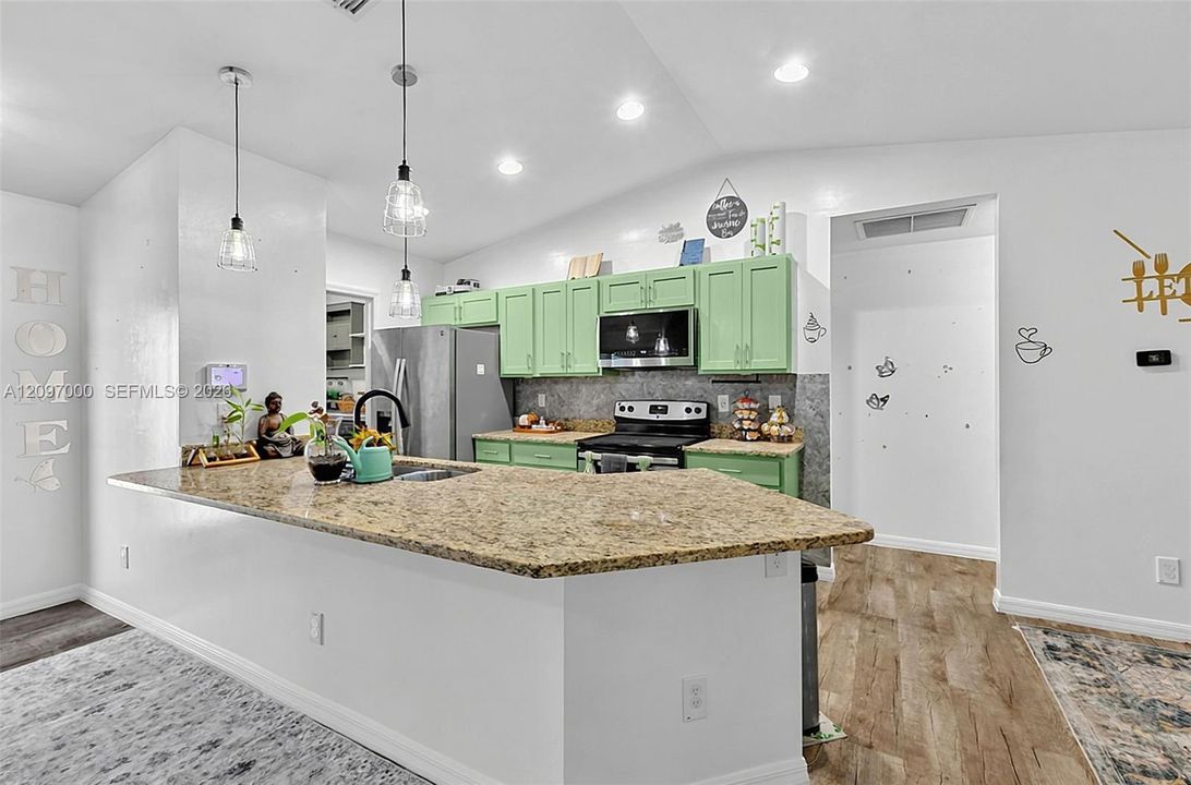 Kitchen featuring a stone-composite breakfast bar, stainless steel appliances, vibrant cabinetry, recessed lighting, and wood-finish flooring