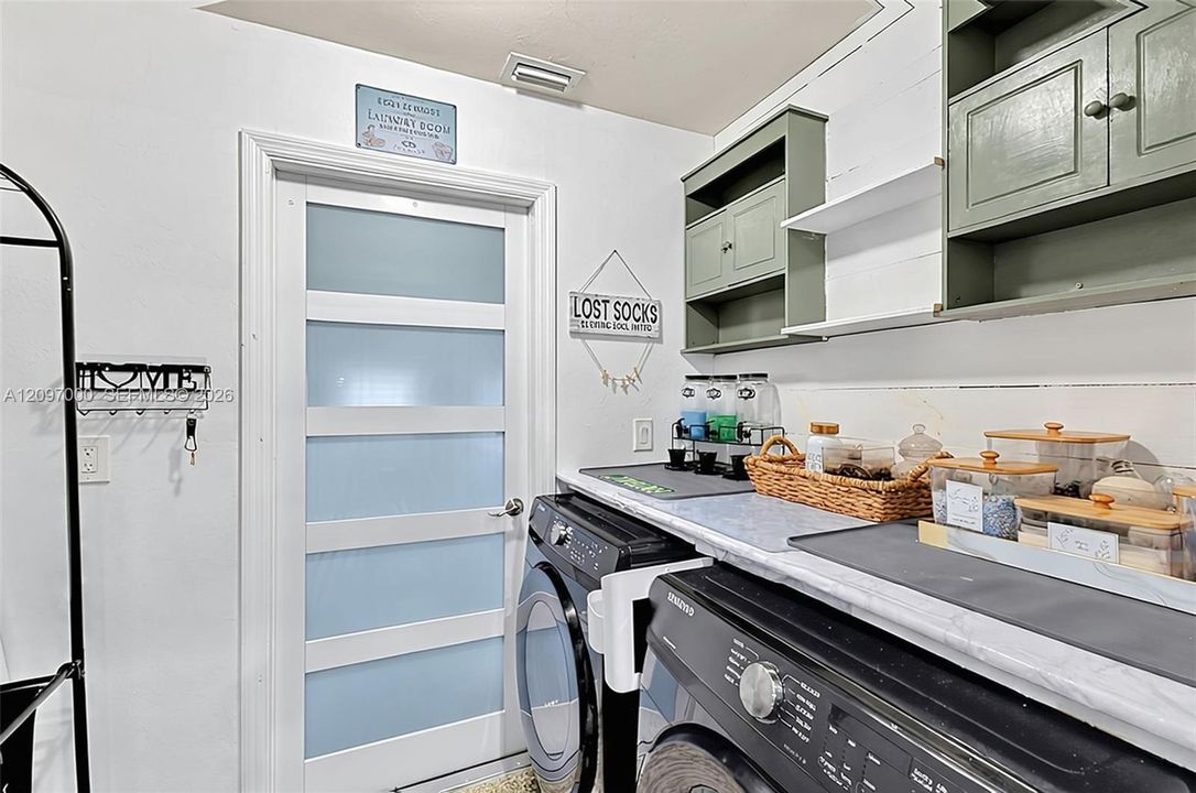 Laundry room featuring a door with frosted glass panels, built-in sage green cabinetry, open shelving, and a solid-surface countertop