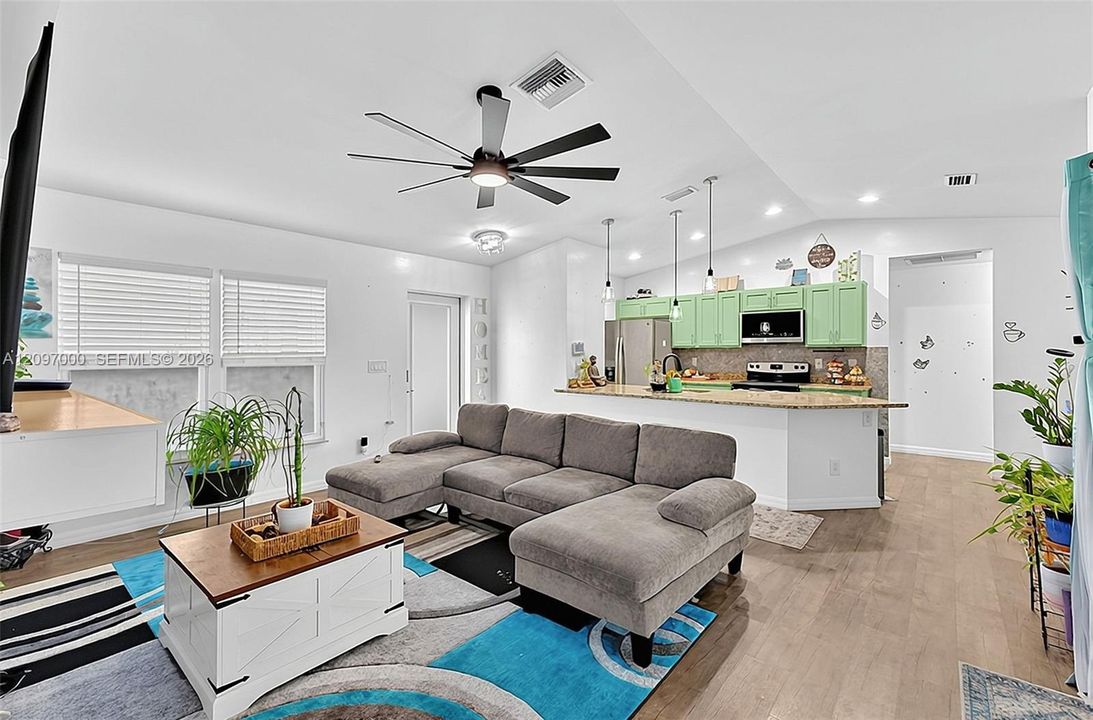 Open-concept interior featuring wood-finish flooring, vaulted ceilings with a multi-blade ceiling fan, a kitchen island with stone countertop, and pendant lighting
