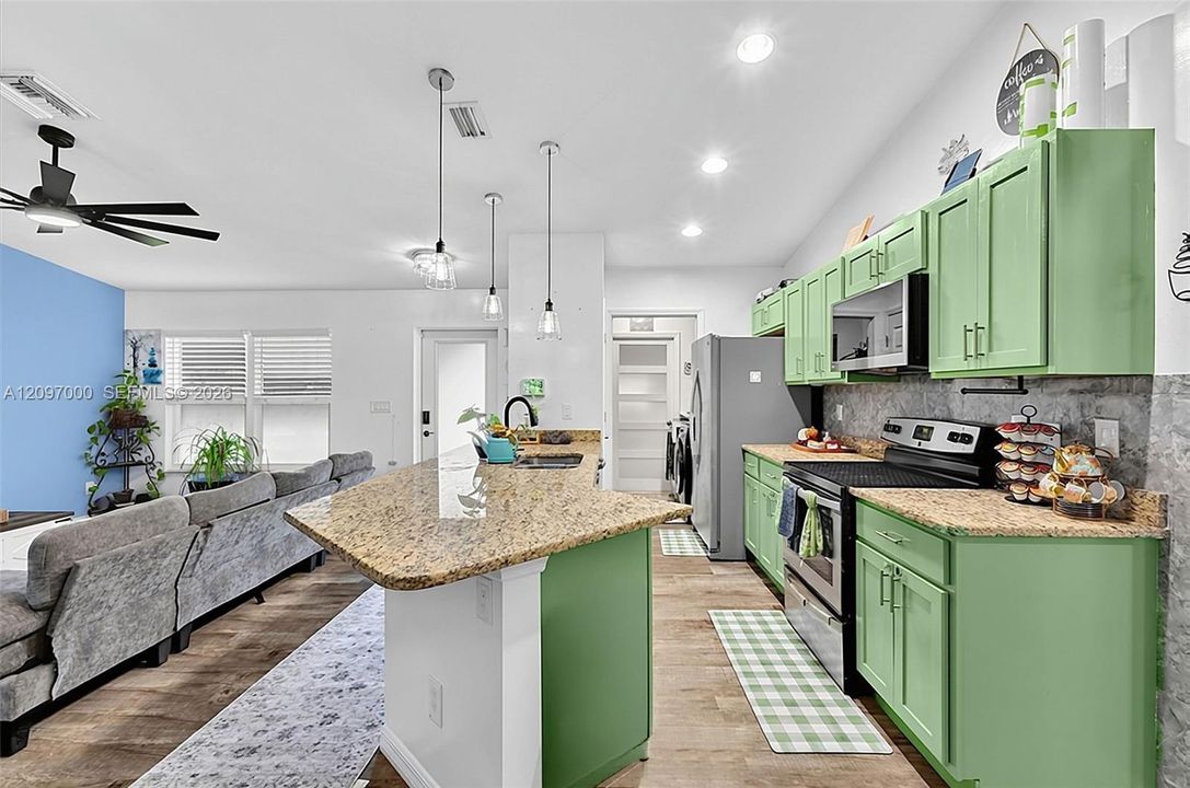 Kitchen featuring custom green cabinetry, stone-finish countertops, stainless steel appliances, wood-finish flooring, and pendant lighting