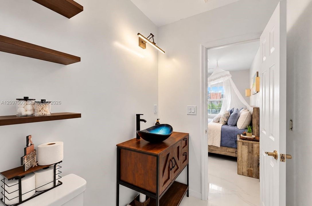 Bathroom featuring a vanity with wood-finish cabinetry, metal frame, and vessel sink, accompanied by floating wood-finish shelving and a linear wall-mounted light fixture